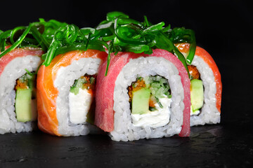Delicious uramaki sushi rolls covered with chuka seaweed on black background