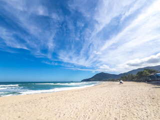 Tropical Shoreline with Ocean Foam and Lush Green Hills Under Blue Sky