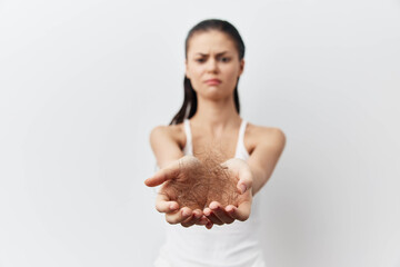 Woman showing frustration with hair loss and holding strands of hair in her hands against a plain...