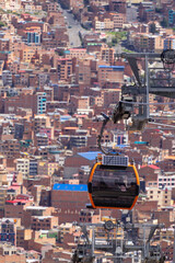 Orange cable car cabin of Mi Teleferico system suspended above dense urban hillside buildings in La...