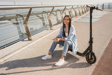 Smiling woman holding smartphone using mobile app for electric scooter rental while has excursion...