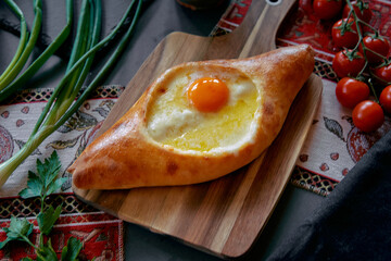 A Deliciously Baked Georgian Khachapuri with an Egg and Melted Cheese on a Wooden Board Surrounded...