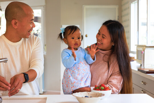 Proud parents watching toddler clapping and smiling in kitchen - Powered by Adobe