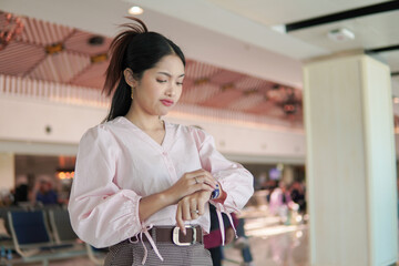 Pretty young Asian woman checking time on watch, feeling upset while waiting in an airport lounge.