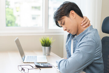 Body muscles stiff problem, ache asian young man pain neck and shoulder while sitting work on chair at home, male holding massaging rubbing, hurt or sore body. Healthcare people, office syndrome.
