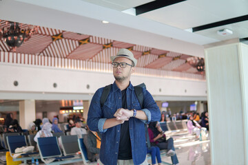 Handsome young Asian man checking time on watch, feeling upset while waiting in an airport lounge.
