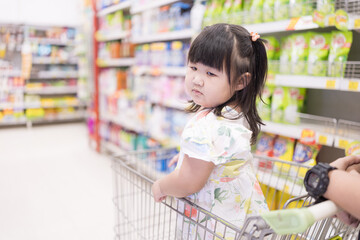 A little girl is sitting in a shopping cart in a shopping mall,Shopping with children. Buying, preparing and cooking food for the holidays. 