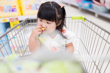 A little girl is sitting in a shopping cart in a shopping mall,Shopping with children. Buying,...