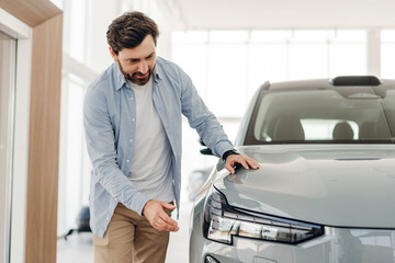 Customer, happy Latin bearded man examining new car in dealership showroom