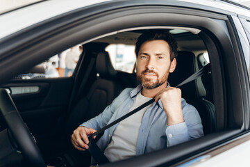 Smiling handsome middle aged man fastening seat belt while sitting in car