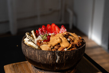 Gesunde Acai Bowl mit frischen Fr&uuml;chten, Granola und Erdnussbutter in einer Kokosnussschale