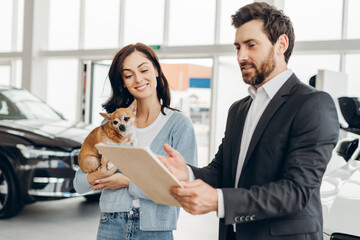Car salesman showing contract to woman holding dog in dealership