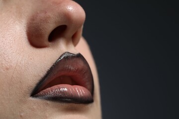 Fototapeta premium Beautiful young woman with black lip liner on dark grey background, closeup. Space for text