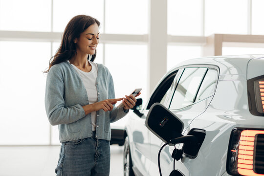 Customer using smartphone while charging electric car at dealership - Powered by Adobe