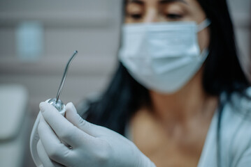 Female dentist with gloves holding a dental tool, ready for patient care, in a modern clinic.
