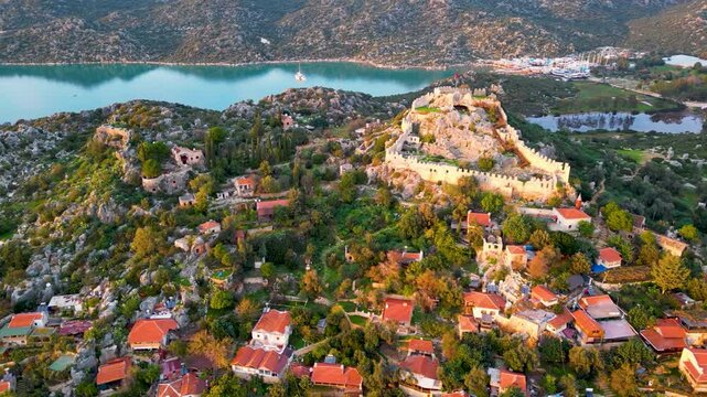 Aerial view of the Castle of Simena and the coastal village on the Mediterranean Sea, Antalya Province, Turkey. Calm sea, ancient ruins, and sunset light over the island and fortress.