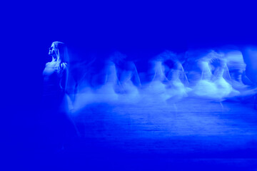 This image captures a woman in motion, seemingly dancing or twirling with a piece of white fabric against a dark background. The fabric and parts of the woman appear somewhat blurred, 