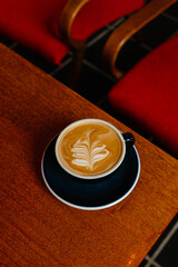 Cappuccino with plant based milk in a large mug on a wooden table. A cup of coffee against the background of cozy red armchairs. Specialty coffee concept