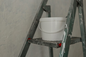 Plastic jar with white wall paint on a stepladder. Process of painting walls in a room