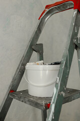 Plastic jar with white wall paint on a stepladder. Process of painting walls in a room