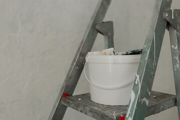Plastic jar with white wall paint on a stepladder. Process of painting walls in a room