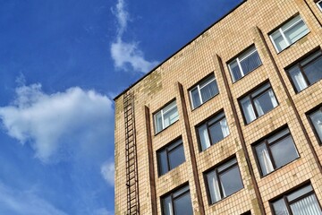 Fototapeta premium A low-angle view of a Soviet-style brick building against a bright blue sky with fluffy white clouds. Urban architecture in Eastern Europe.