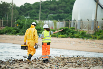 Workers in safety gear walking to survey at site near refinery storage tanks, industry facility, Hazardous environment, scientist holding toolbox, woman with laptop