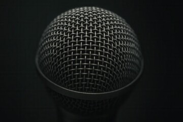 A close-up of a metallic microphone with a dark background, highlighting its intricate mesh pattern