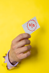 Male hand coming out of a torn yellow paper holding a percentage tag, discount and promotion concept