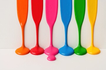A vibrant array of paint-splattered glasses in a row, each filled with a different color, stands against a pristine white background