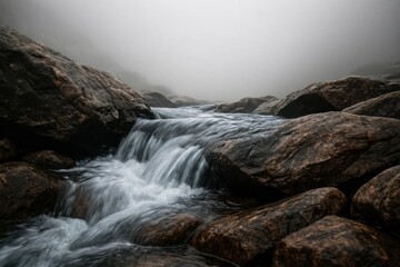 Obraz premium A serene river meanders through a foggy landscape, its waters flowing over moss-covered rocks