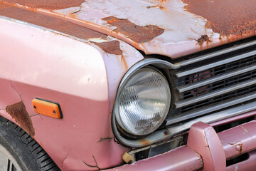 The car headlights of abandoned old rusty car on the side of the road.