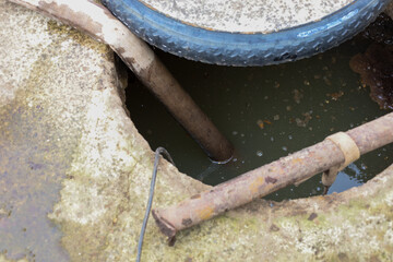 An abandoned drainage hole containing dirty water, old pipes, and parts of a bicycle wheel. This...