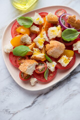 Plate with tuscan-style tomato and bread salad or panzanella, vertical shot on a white stone background, middle close-up