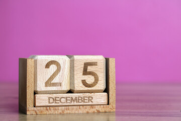 Wooden perpetual calendar showing the date of december 25th on pink background