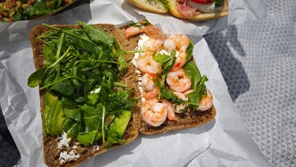 Open-faced sandwich with shrimp, arugula, avocado, and cheese on whole grain bread. This image represents healthy eating, freshness, and gourmet outdoor dining