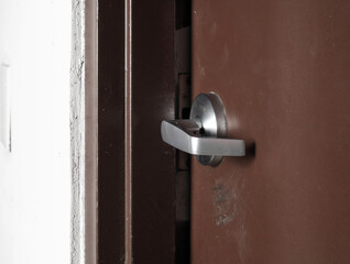 Heavy door lock broken. Commercial fire door or emergency exit door in building. Door lock or latch damaged and stays open. Fire risk and safety issue. Locksmith or repairman needed. Selective focus.