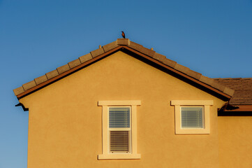Stucco-finished residential house exterior with gable roof, double-pane windows, and roof tiles, illustrating typical suburban housing architecture and building materials in modern home construction