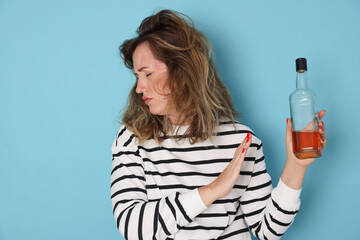 Woman with bottle of alcoholic drink suffering from hangover on light blue background