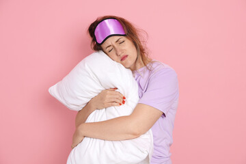 Woman with pillow suffering from hangover on pink background