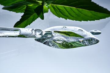 A pipette with a drop of serum in refreshing mint leaves.
