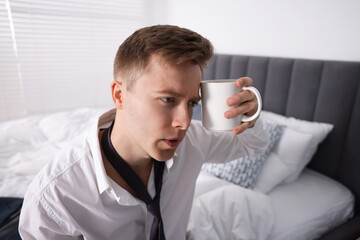 Sad young man with cup of coffee getting ready at home