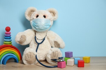 Pediatrician concept. Toys, medical mask and stethoscope on wooden table against light blue...