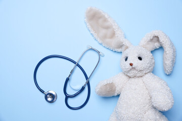 Pediatrics concept. Toy bunny with stethoscope on light blue background, top view. Space for text