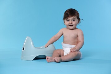 Cute little baby sitting near potty on light blue background