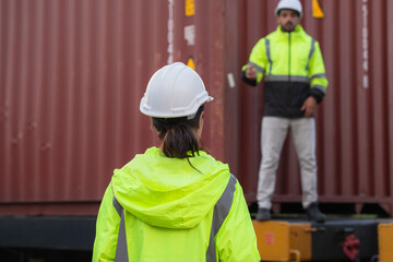 Foreman checking inventory or task details on freight train cars and shipping containers. Logistics concept, import, and export industries.