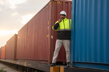 Foreman checking inventory or task details on freight train cars and shipping containers. Logistics...