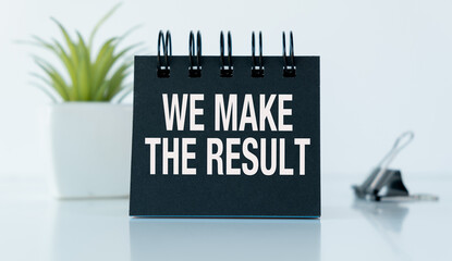 A black notebook with the words We Make the Result written on it. The notebook is on a table
