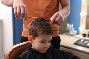 Professional barber cutting boy's hair in barbershop, closeup