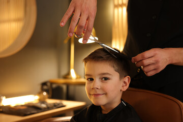 Professional barber cutting boy's hair in barbershop, closeup. Space for text